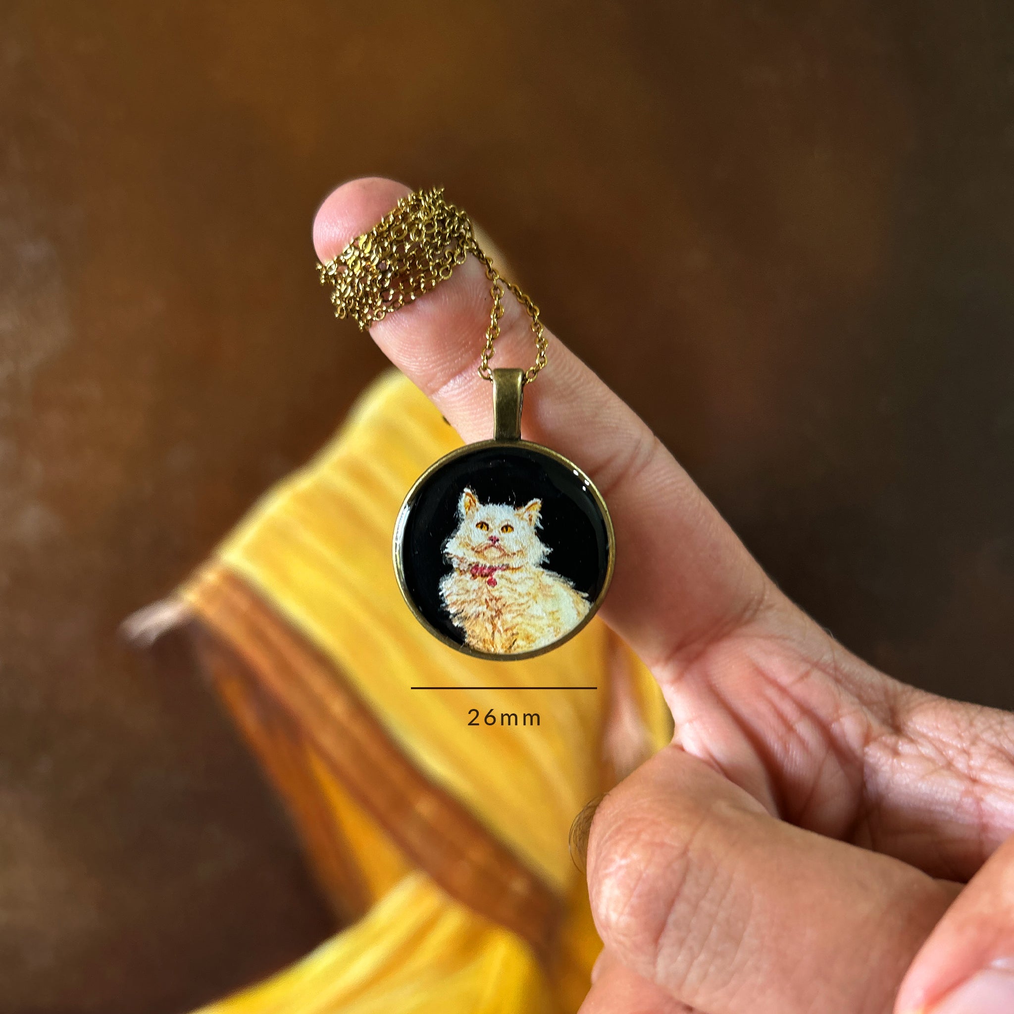 Expertly painted petite portrait (26mm) showcasing majestic Persian cat's regal bearing, with fluffy white fur and distinctive red-pink collar delicately rendered against dramatic black background. This legacy memento, held between fingers with golden chain gracefully draped, floats before artist's original oil painting in warm amber tones. Each brushstroke captures precious companion's noble expression, preserved with museum-grade sealant in this generational keepsake.