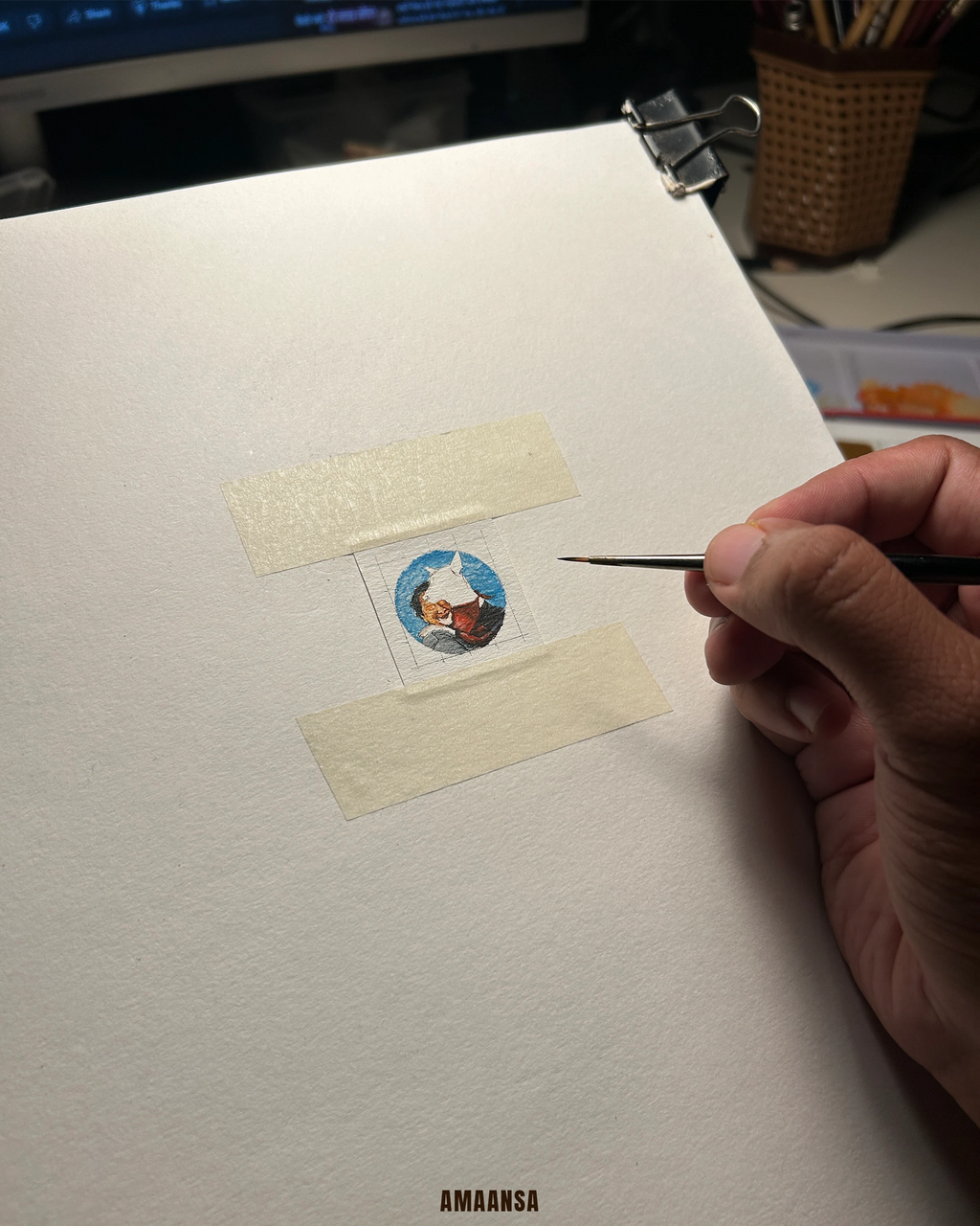 artist using a small brush on a piece of paper with a small illustration, in an indoor setting.