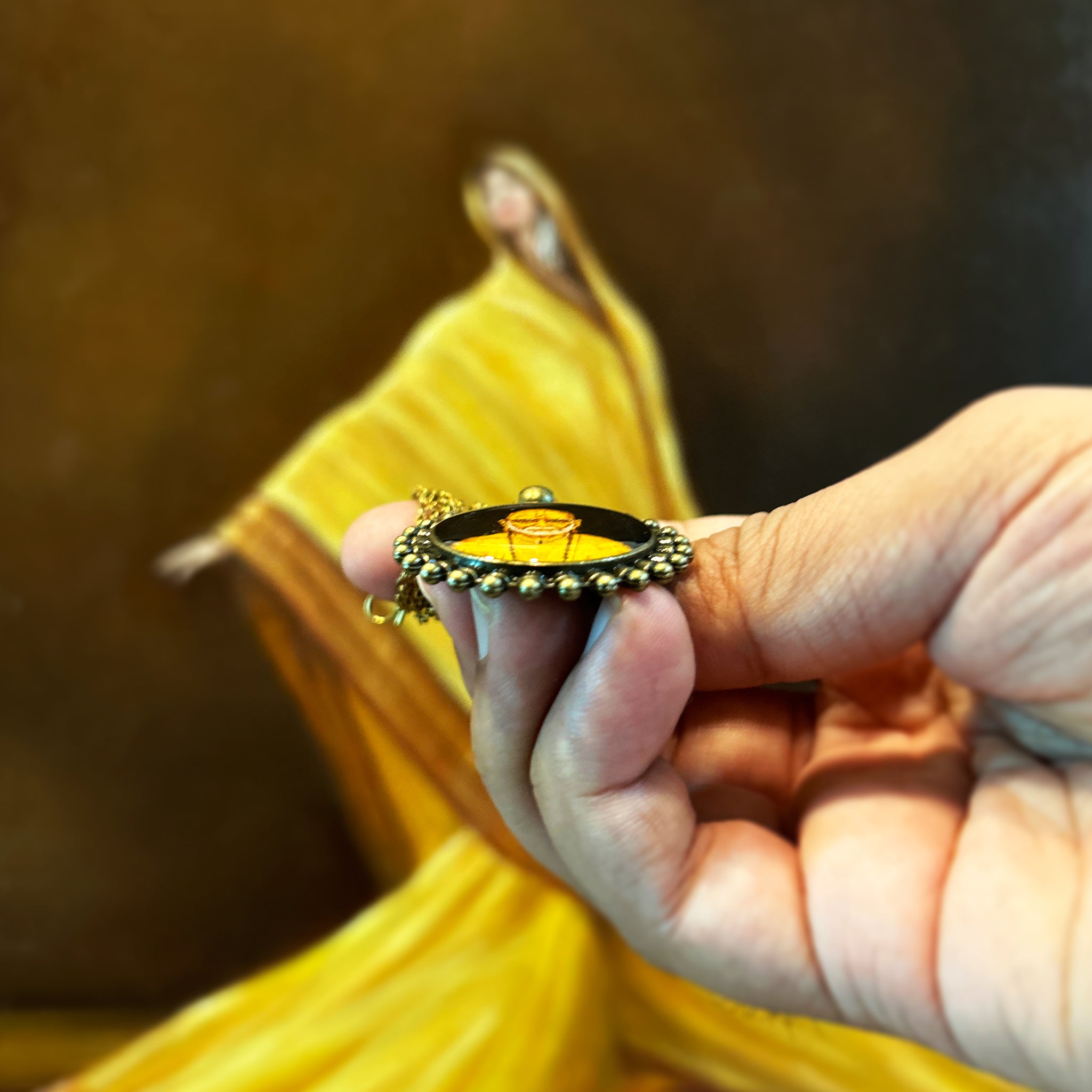 AMAANSA's devotional art pendant (26mm) featuring revered Swami Samartha's miniature portrait, intricately painted. Sacred medallion nestled between thumb and forefinger to showcase the unique dimensional effect, framed by our signature Pearl Border (Pathakkam Moti) in antique brass finish. Antique gold colored chain gracefully held, set against artist's oil painting featuring flowing yellow fabric. Protected by crystal-clear sealant, this sacred keepsake offers a tangible connection to divine.