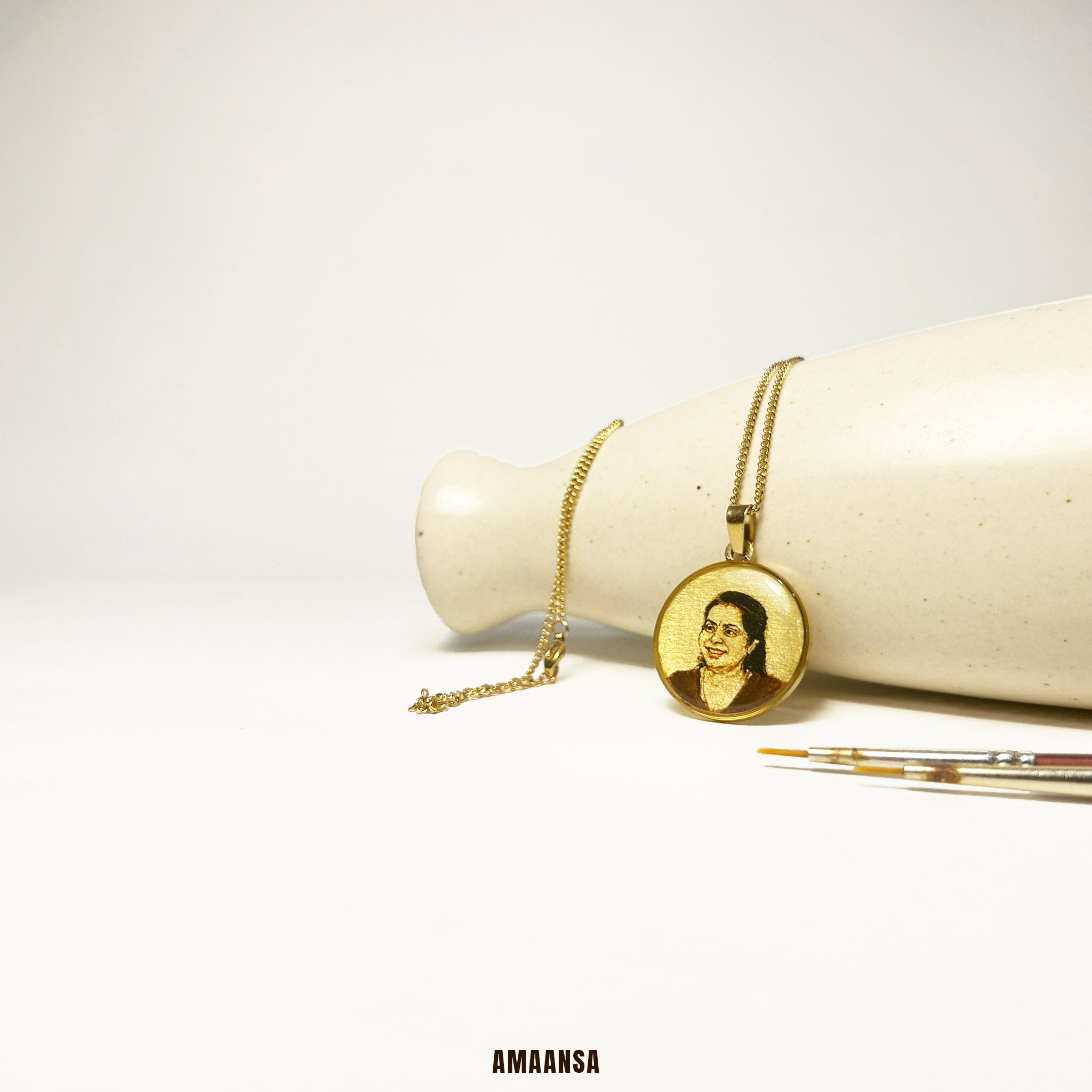 18k Gold plated necklace with a portrait painting pendant on a white surface, featuring the brand 'AMAANSA'.